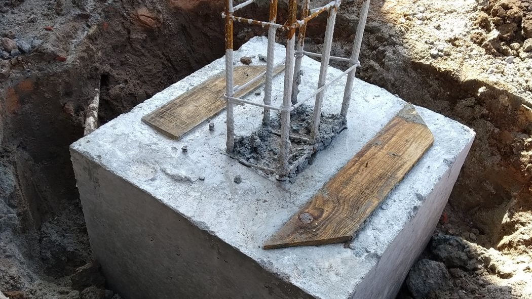 Bloco de fundação de concreto em escavação, com armadura de arranque de pilar e dois sarrafos de madeira sobre a face superior