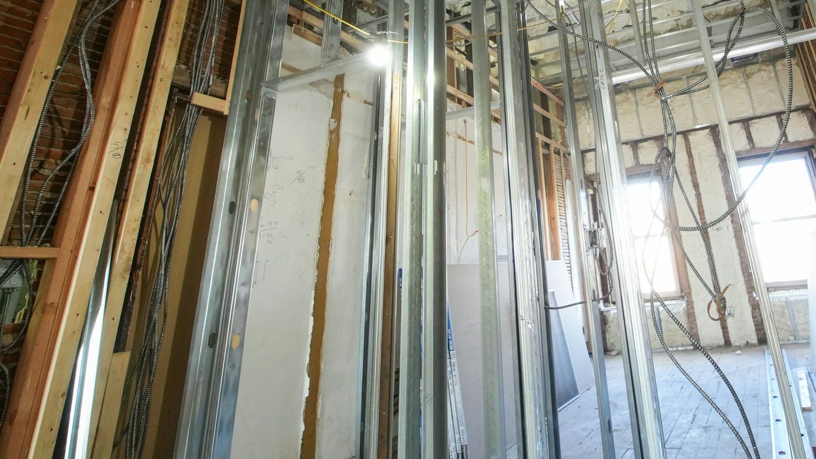 Montantes metálicos de parede de drywall em obra, com placas de gesso encostadas e parede antiga de tijolos à esquerda