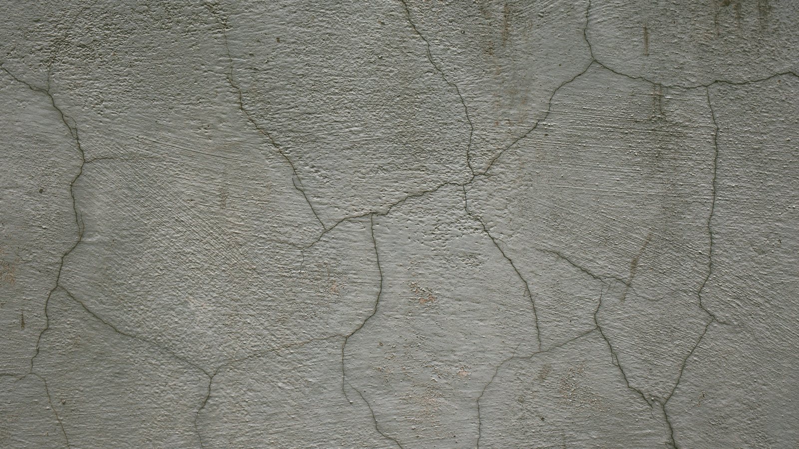 Parede de reboco cinza com fissuras finas ramificadas que se cruzam em desenho de mapa, sem direção definida