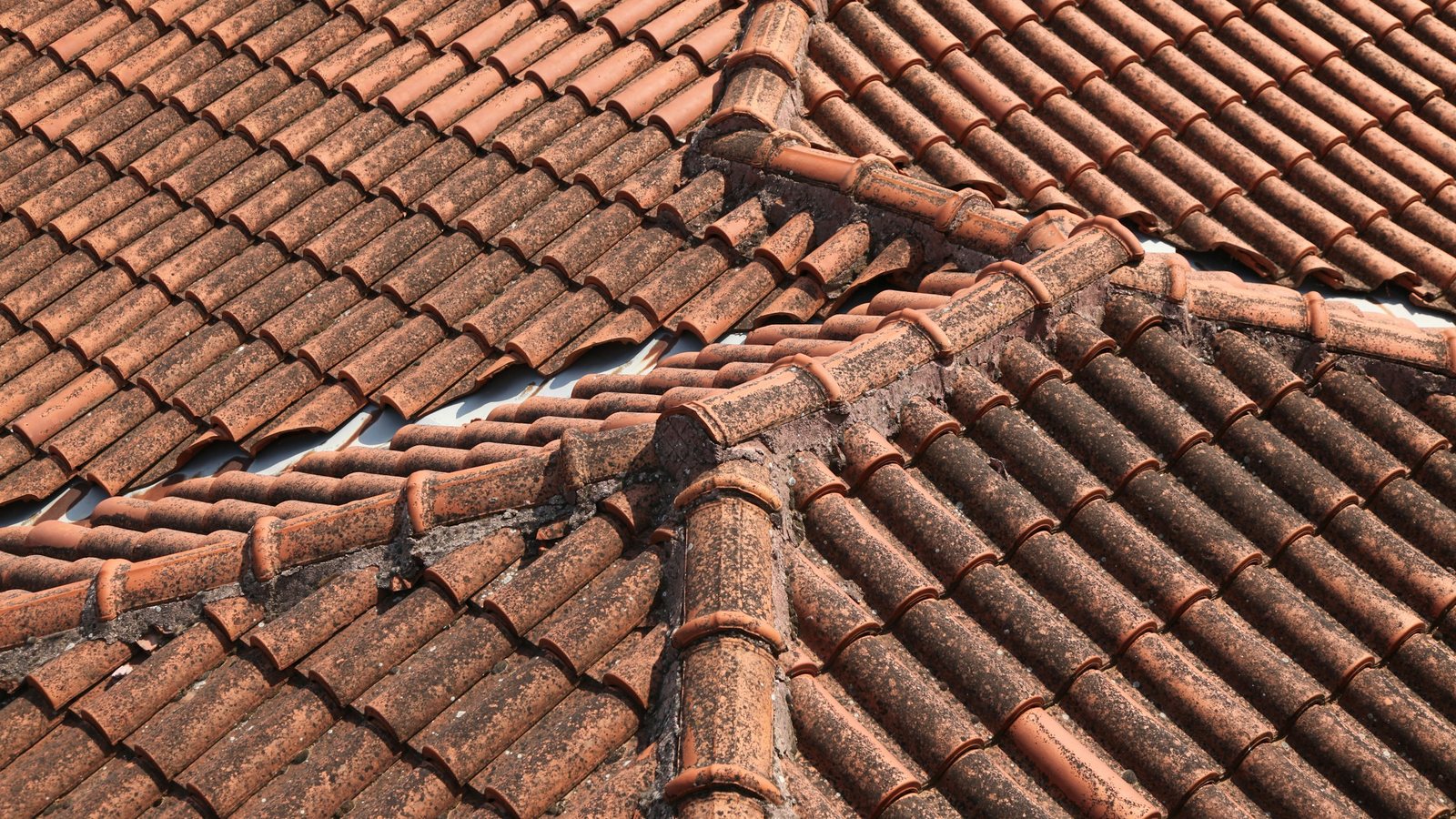 Telhado de telhas cerâmicas visto de cima, com cumeeira e espigões argamassados se encontrando e um vão aberto entre dois panos