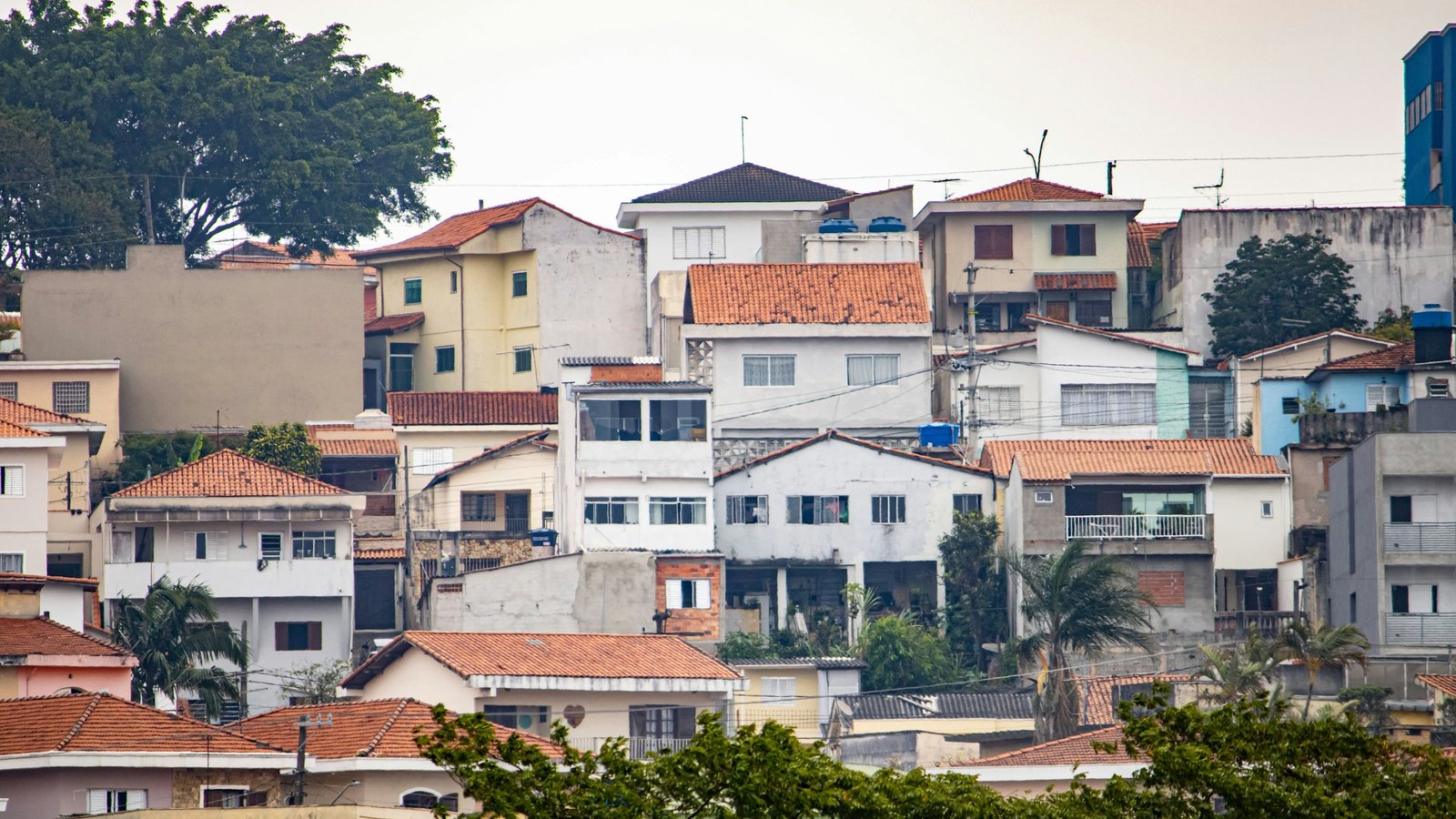 Bairro residencial em encosta, com sobrados de alvenaria rebocados e pintados, telhados de telha cerâmica e árvores entre as casas