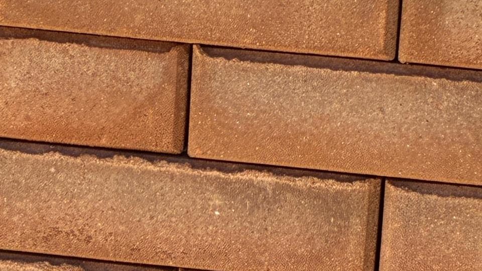 Tijolos prensados de cor terrosa empilhados em fiadas alternadas, com a face lisa e textura granulada